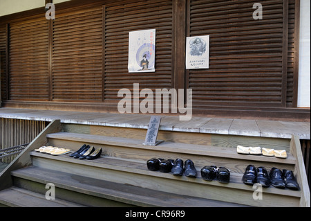 Zori-Rasen Sandalen, High Heels Damenschuhe, klobige schwarze Schuhe von einem Priester und schwarze Herrenschuhe vor einer hölzernen Tür Stockfoto