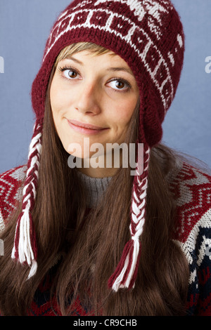 Hübsche junge Frau mit einem leichten Lächeln tragen Mütze mit Norwegermuster. Studioportrait gegen einen hellblauen Hintergrund Stockfoto