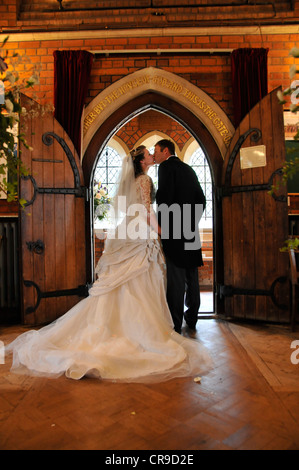 Braut und Bräutigam küssen in gewölbte Tür der Kirche zeigt die Rückseite des fabelhaften Kleid. Stockfoto