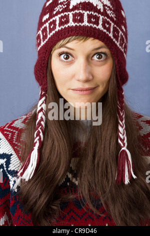 Hübsche junge Frau mit Wolle Mütze schaut in die Kamera überrascht. Lustiger Winter Mode Porträt gegen einen hellblauen Hintergrund Stockfoto