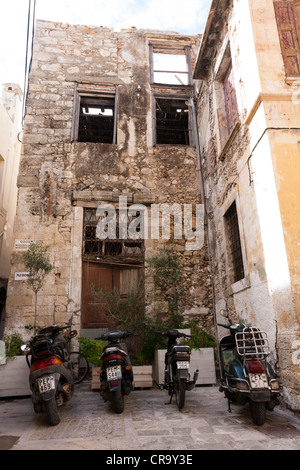 Mopeds geparkt auf kleinstem Raum vor einem semi-verlassener Gebäude auf einer Gasse in Rethymnon, Crete Stockfoto