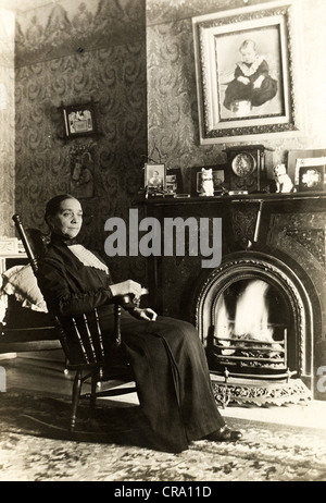 Alte Dame in viktorianischen Salon vor brüllenden Feuer sitzen Stockfoto