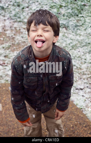 Ein kleiner Junge steckt seine Zunge Schneeflocken zu fangen versuchen Stockfoto