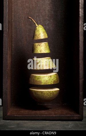 Eine Birne, die ist in Kapitel unterteilt und in einer Holzkiste auf einem Schieferoberfläche zu schweben scheint. Stockfoto