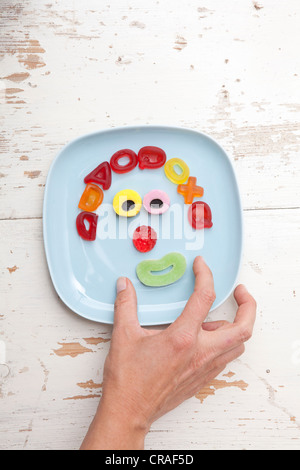 Hand Griff nach Süßigkeiten, Gesicht aus Gummibärchen, Essen für Kinder Stockfoto