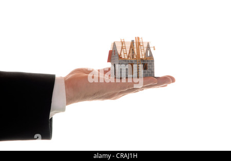 Des Mannes Hand, die ein Modell für ein Haus, symbolisches Bild für Hypotheken Stockfoto