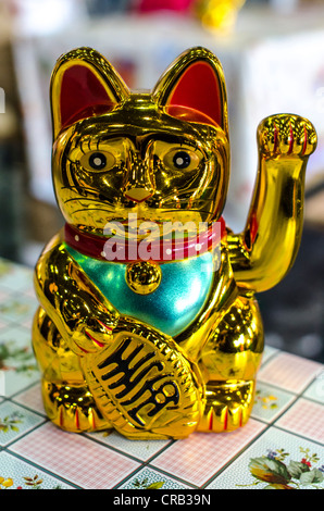 Goldene, glänzende Kunststoff winken Katze ("lucky Cat") auf Tisch mit Tischdecke. Stockfoto