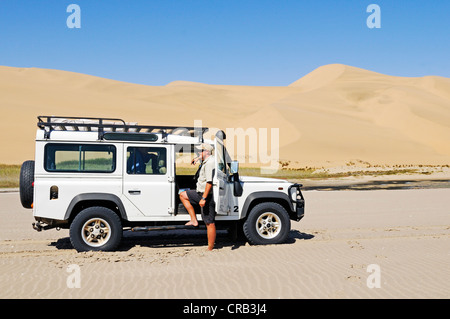 Mann mit einem Landrover Defender Geländewagen in den Feuchtgebieten von Sandwich Harbour, Namib-Naukluft-Nationalpark Stockfoto