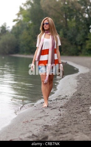 Junge Frau mit Sonnenbrille zu Fuß an einem Sandstrand Stockfoto