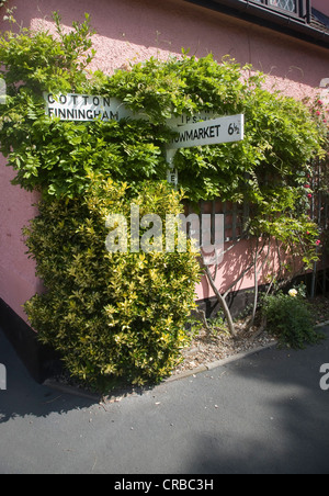 Dorf Richtung Straßenschild überwuchert an Hauswand Mendlesham, Suffolk, England Stockfoto