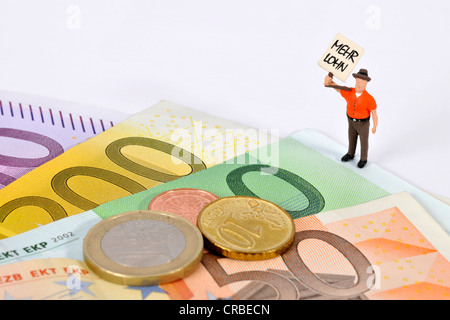 Miniatur-Figur mit einem Schild, Mehr Lohn, Deutsch für mehr zahlen, neben Euro-Banknoten und-Münzen Stockfoto