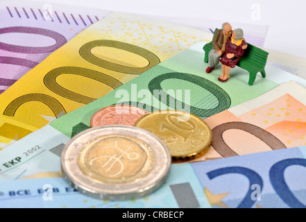 Miniatur-Figuren von einem Ehepaar im Ruhestand sitzt auf einer Parkbank auf Euro-Banknoten und Münzen, symbolisches Bild für den Ruhestand Stockfoto