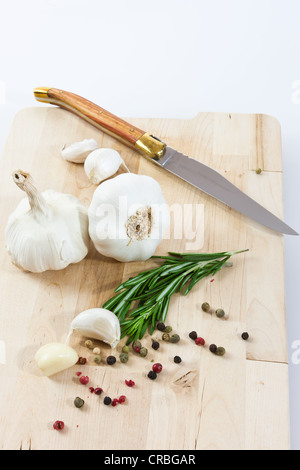 Knoblauch (Allium Sativum) auf einem Holzbrett mit Messer, Rosmarin und schwarzen und roten Pfeffer Stockfoto