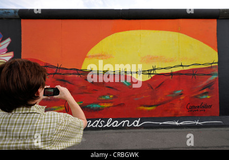 Touristen, die mit dem Fotografieren der Kunst und der Berliner Mauer, Sonnenaufgang im Osten hinter Stacheldraht, Malerei auf einem anderen Segment Stockfoto