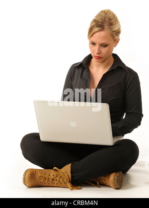 Junge Frau arbeitet an einem Laptop-Computer, sitzt im Schneidersitz Stockfoto
