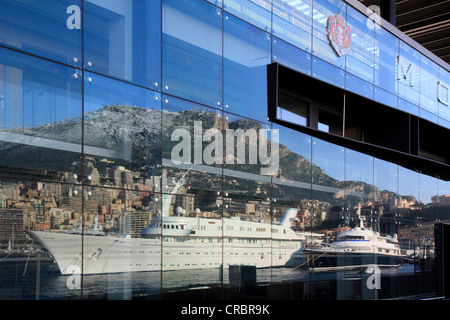 Reflexion an der Fassade des Kreuzfahrtterminals von Port Hercule mit Motoryachten, Atlantis II und The One Stockfoto