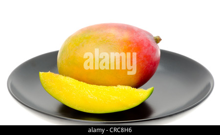 Frische Mango-Frucht mit einer Scheibe von Mango auf einem schwarzen China Teller. Studio mit einem weißen Hintergrund gedreht. Stockfoto