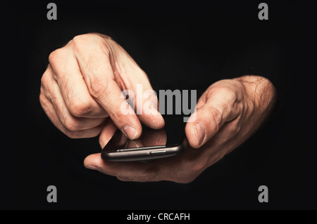 Mann im schwarzen Hemd tippt eine SMS-Nachricht auf seinem Smartphone, schließen Sie herauf Bild, konzentrieren sich auf Händen und das Telefongerät. Stockfoto