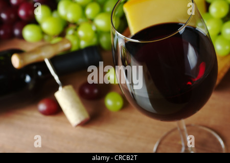 Rotwein im Glas Wein, Trauben, Käse, eine Flasche Wein und einen Korkenzieher mit Korken im Hintergrund Stockfoto