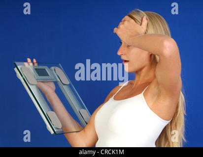 schockiert blonde Frau betrachten die Waage in der hand Stockfoto
