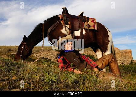 Cowgirl liegen in der Wiese, ihr Pferd stand neben ihr, Saskatchewan, Kanada Stockfoto