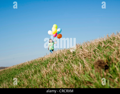 Mädchen läuft in Wiese mit Luftballons Stockfoto