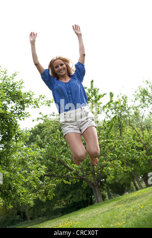Blonde junge Frau springt in Wiese Stockfoto