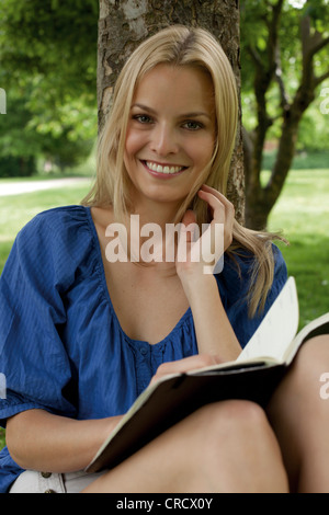 Lesebuch der blonde junge Frau an einem Baum Stockfoto