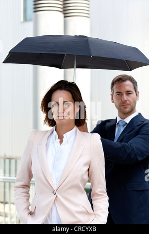 Geschäftsmann Holding-Dach oberhalb Geschäftsfrau Stockfoto