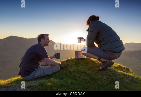 Ein paar genießen einen Chat und ein heißes Getränk den Sonnenuntergang über Lake Buttermere im Lake District. Stockfoto