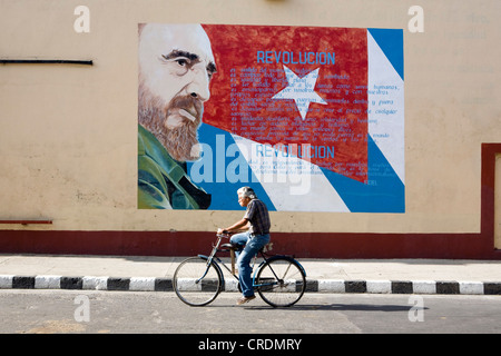 Alten Radfahrer Radsport vor revolutionärer Propaganda auf der Fassade mit Bild von Fidel Castro, Cienfuegos, Kuba Stockfoto