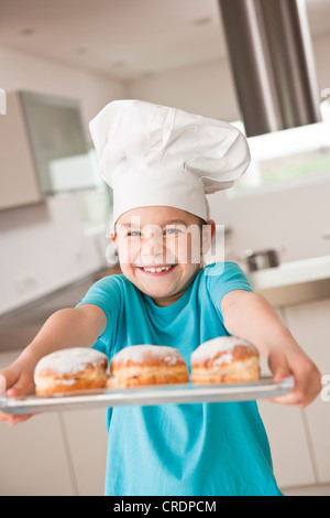 Mädchen mit Kochmütze lachend präsentieren einen Berliner oder Krapfen gefüllt Stockfoto