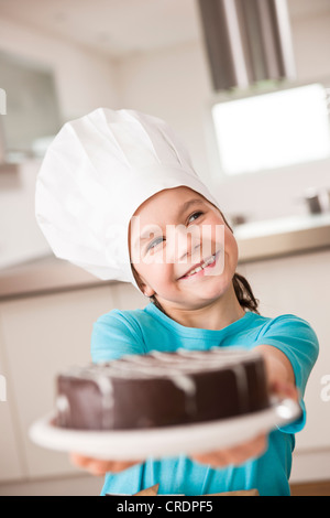 Mädchen in eine Kochmütze präsentiert einen Schokoladenkuchen Stockfoto