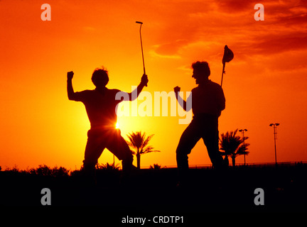 GOLFER, DIE NACH DEM SCHUSS AUF LOCH WÄHREND DES SONNENUNTERGANGS ZU FEIERN Stockfoto