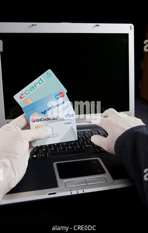 Hacker einen Laptop verwenden, hält eine Krankenversicherungskarte und Kreditkarten und Latexhandschuhe tragen, hinterlassen keine Spuren, symbolische Stockfoto