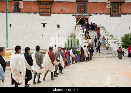 Tibetisch-buddhistische Festival Gewand Menschen tragen die traditionelle Gho stehen in einer Warteschlange, Rinpung Dzong Kloster und Festung Stockfoto