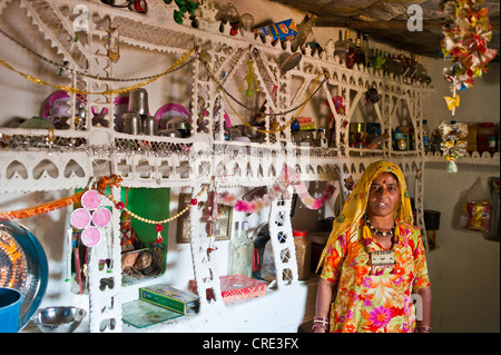 Indische Frau trägt einen traditionellen Sari stehen in ihrer Küche neben einem reich verzierten Regal mit Haushaltsgeräten Stockfoto