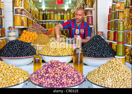 Händler bieten verschiedene Oliven, Olivenöl in Geschirr und Gläser zum Verkauf an seinem Stand, Souk, Basar, Marrakesch, Marokko Stockfoto