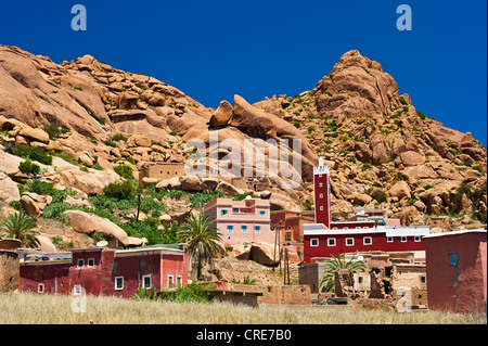 Kleines Dorf mit einer Moschee und Minarett vor einer typischen felsigen Landschaft mit Granitfelsen, Tafraoute Stockfoto