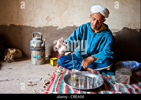 Älterer Berber Mann mit Turban sitzen auf dem Boden auf einem Teppich traditionellen Pfefferminztee mit einer silbernen Kanne gießen Kelaa M'gouna Stockfoto