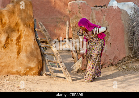 Junge indische Frau trägt einen Sari fegen den Boden vor ihr Hof-Tor mit einem Stroh Besen, Thar-Wüste, Rajasthan, Indien Stockfoto