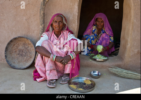 Eine alte indische Frau trägt einen Sari auf dem Boden vor einem Hauseingang sitzen, sitzt eine junge Frau an der Tür Stockfoto