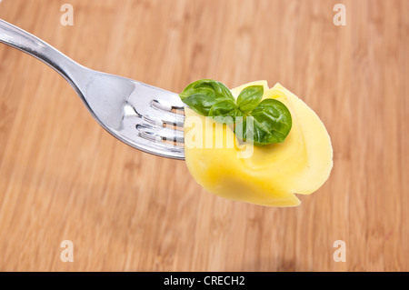 Tortellini auf einer Gabel mit Basilikum auf einem hölzernen Hintergrund Stockfoto