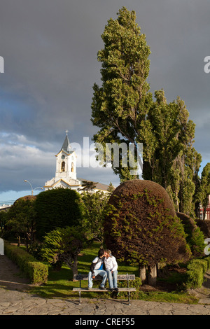 Ein paar Küsse wie die Sonne in einem Stadtpark mit einem Kirchturm im Hintergrund. Stockfoto