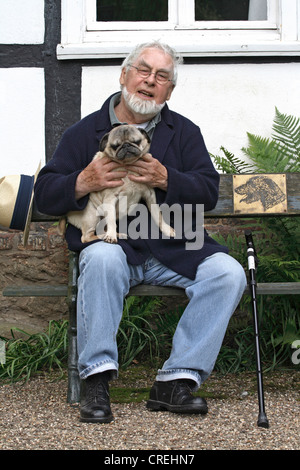 Mops (Canis Lupus F. Familiaris), Alter Mann sitzt auf einer Bank im Garten mit einem Mops, 11 Jahre alt Stockfoto