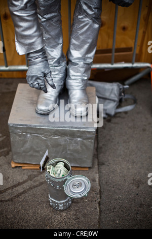 A Street Performer in Silber gekleidet fällt einen Dollarschein in eine Dose. Stockfoto