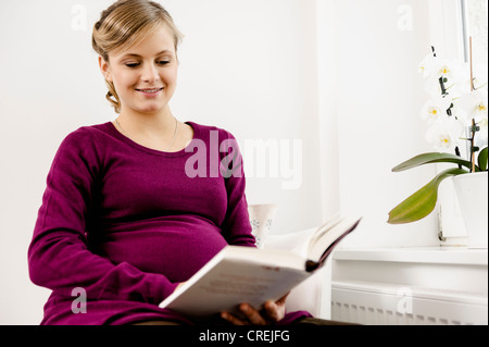 Schwangere Frau im Wohnzimmer lesen Stockfoto