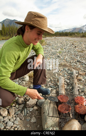 Junge Frau grillenden Hamburgern, BBQ am Lagerfeuer, Kiesbank, Wind River, Yukon Territorium, Kanada Stockfoto