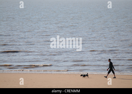 Eine Frau geht ihren Hund in den frühen Morgenstunden entlang des Strandes bei Frinton in Essex Stockfoto