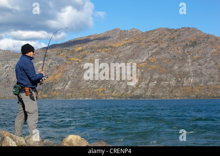 Mann spin Angeln, Kampffische ein, Kusawa See, Bergen im Hintergrund, Indian Summer, Blätter in Herbstfarben, Herbst, Yukon-Territorium Stockfoto